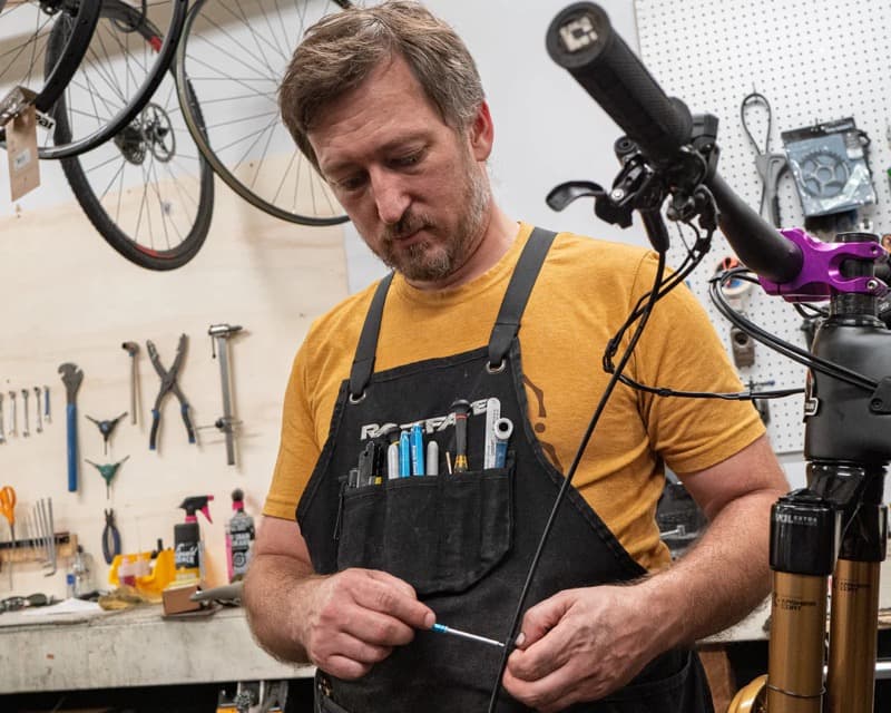 Mecánico de bicicletas con delantal de herramientas reparando una bici